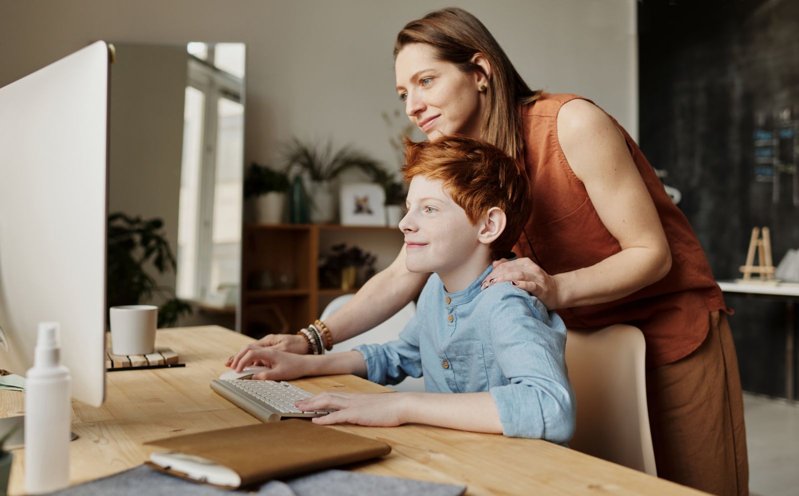 Une éducatrice accompagne un enfant à son bureau, dans un moment de soutien calme et bienveillant à la maison