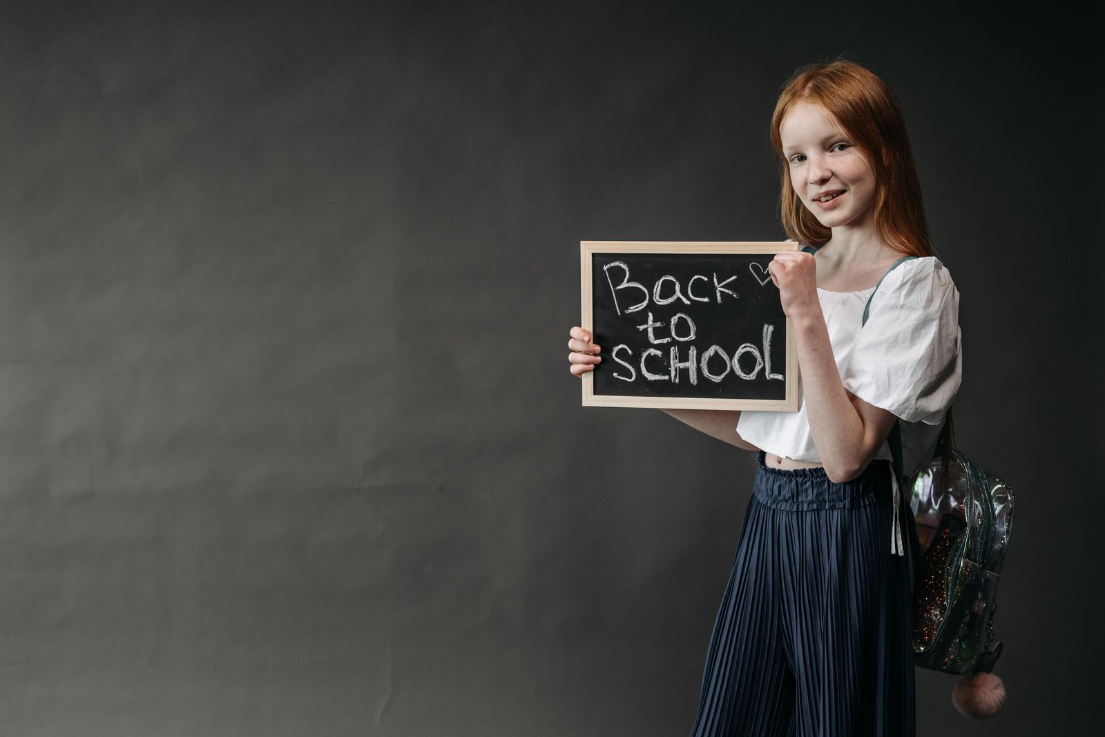 Une fillette souriante avec son cartable, tenant une ardoise « Back to School », prête pour la rentrée